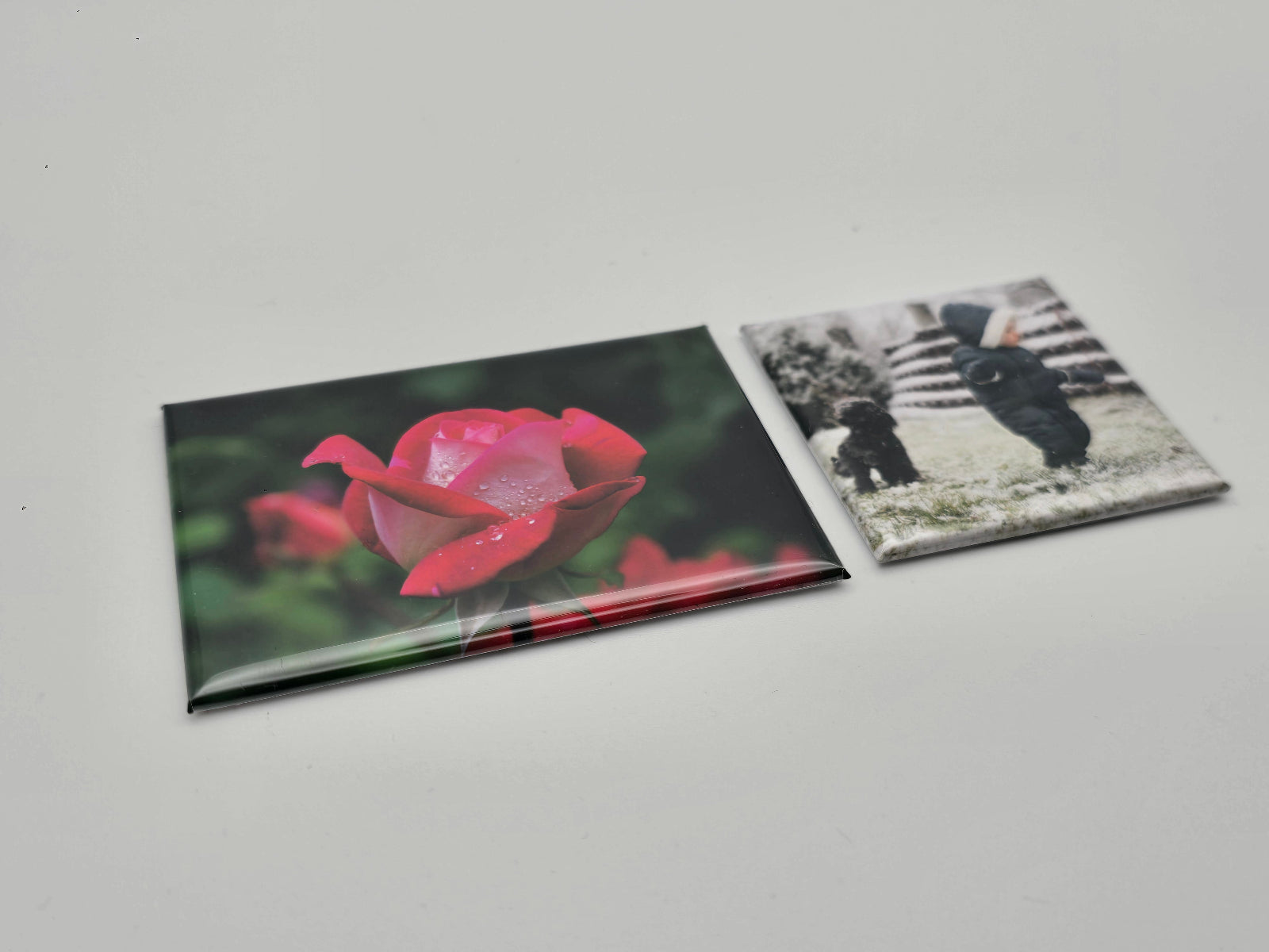 Two photo magnes, one with a pink flower and the other with a black and white image of two people, on a light gray background.