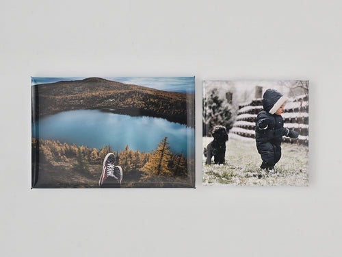 Two framed photo magnets, one of a lake and mountains, the other of a person and dog by a fence.
