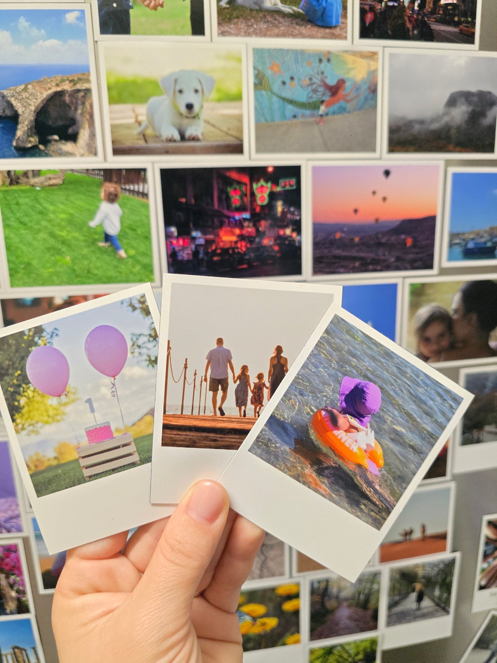 Collection of Polaroid retro magnet photos held by a hand with a collage of various photos in the background.