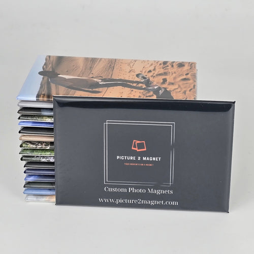 Stack of custom photo magnets with a black packaging box on a gray background